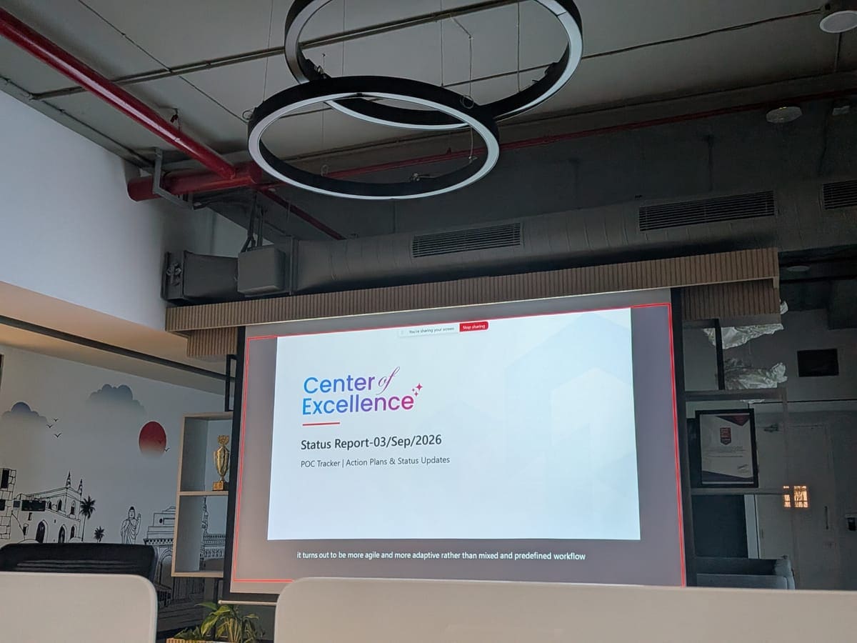 A presenter at the townhall beside a projected Center of Excellence status report