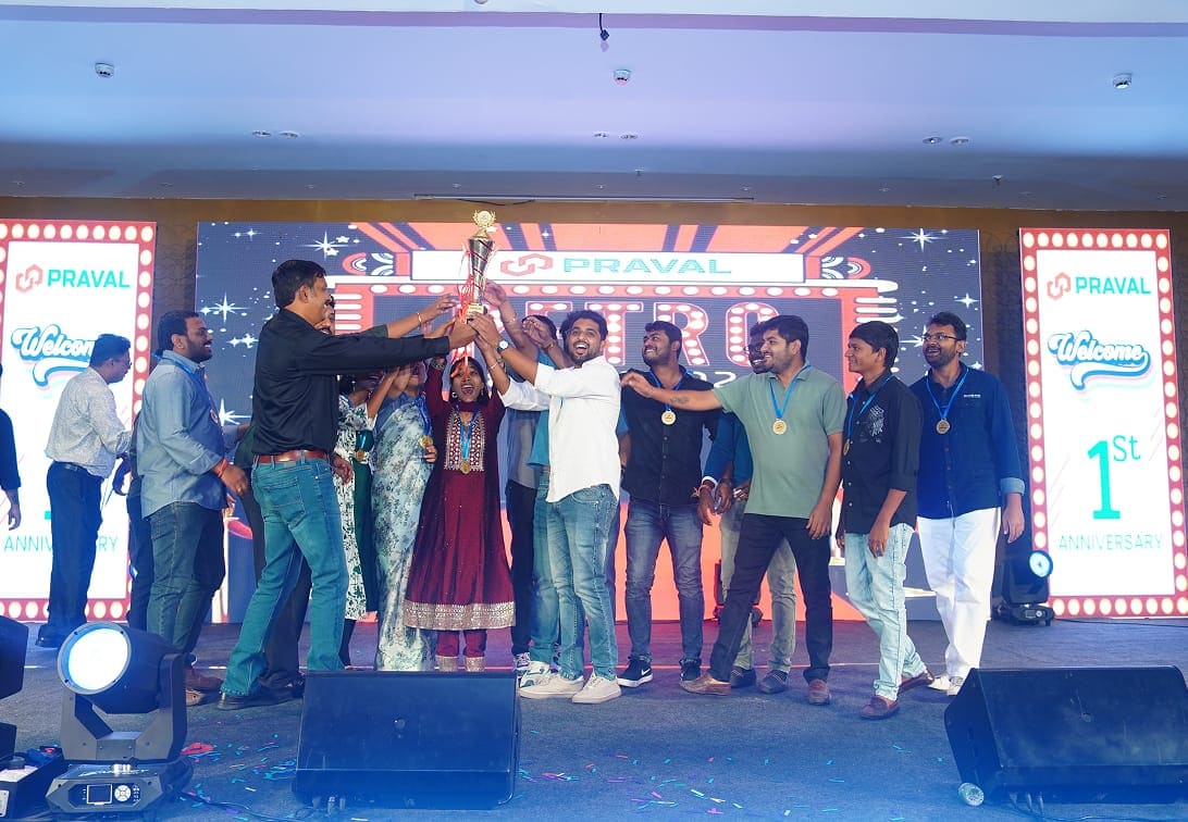 Team members raising a trophy together on stage at Praval's first-anniversary celebration